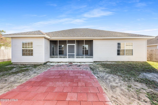 rear view of property with a sunroom, a shingled roof, and fence