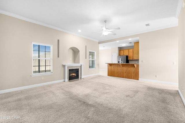 unfurnished living room with light carpet, ceiling fan, baseboards, and ornamental molding