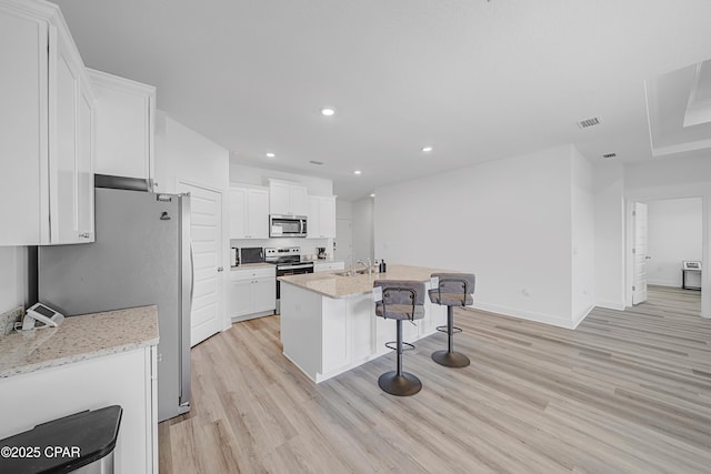 kitchen with white cabinetry, a kitchen bar, a kitchen island with sink, stainless steel appliances, and light stone countertops