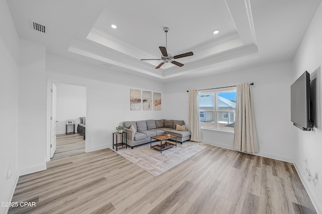 living room with crown molding, a raised ceiling, ceiling fan, and light wood-type flooring