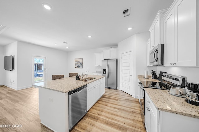 kitchen featuring sink, stainless steel appliances, light stone counters, an island with sink, and white cabinets