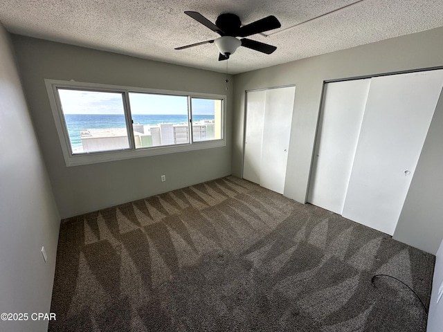 unfurnished bedroom featuring ceiling fan, carpet flooring, multiple closets, a textured ceiling, and a water view