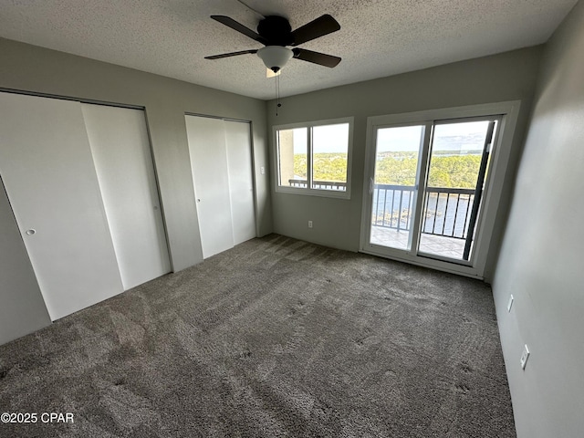 unfurnished bedroom with ceiling fan, two closets, a textured ceiling, and carpet floors