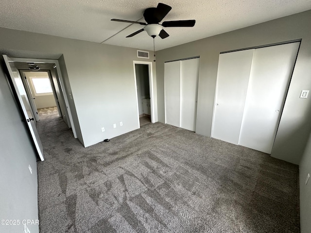 unfurnished bedroom featuring a textured ceiling, ceiling fan, carpet, and two closets