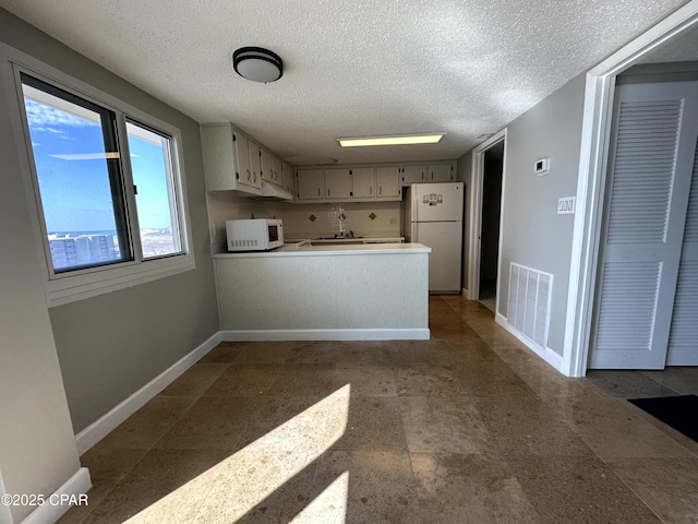 kitchen with sink, white appliances, kitchen peninsula, and a textured ceiling