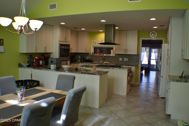 kitchen featuring light tile patterned flooring, white cabinetry, island range hood, appliances with stainless steel finishes, and light stone countertops