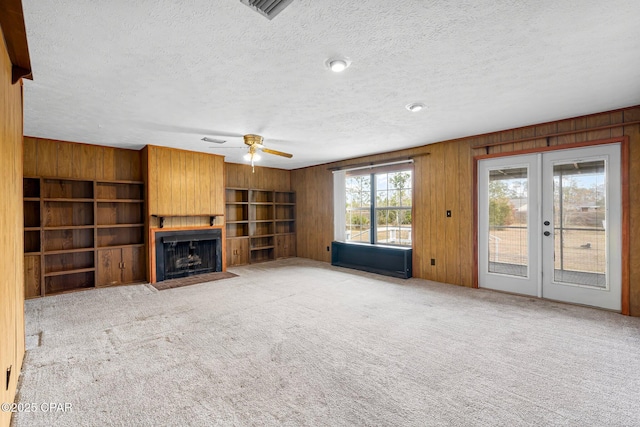 unfurnished living room with a textured ceiling, light carpet, french doors, a large fireplace, and ceiling fan