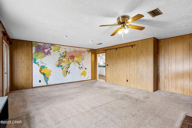 carpeted spare room featuring a textured ceiling, ceiling fan, and wood walls