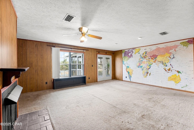 unfurnished living room with ceiling fan, light carpet, wood walls, and french doors