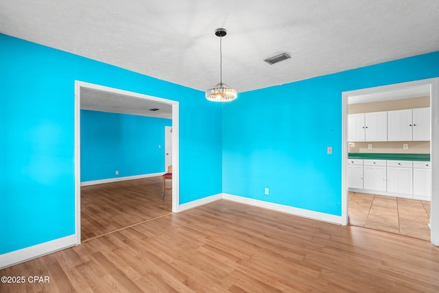 empty room with a textured ceiling, a notable chandelier, and light wood-type flooring