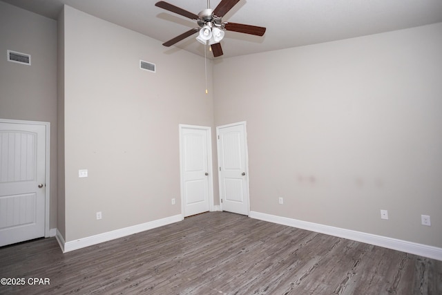 unfurnished room with dark wood-type flooring, a towering ceiling, and ceiling fan