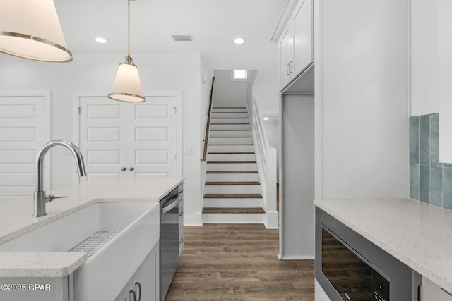 kitchen with pendant lighting, dishwasher, white cabinetry, sink, and light stone counters