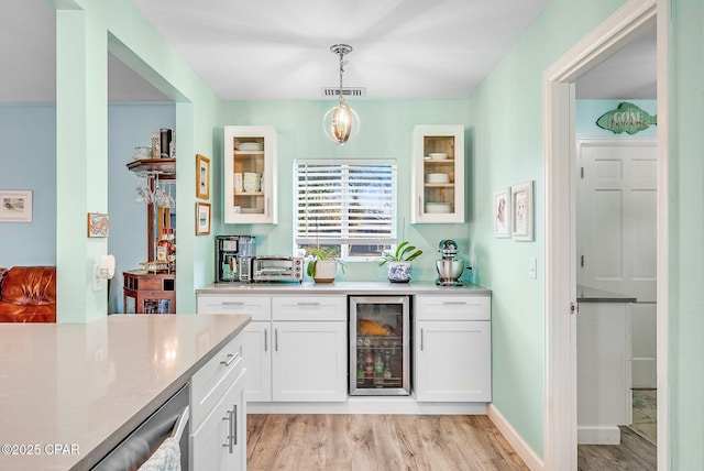 interior space featuring white cabinets, pendant lighting, beverage cooler, and light hardwood / wood-style flooring