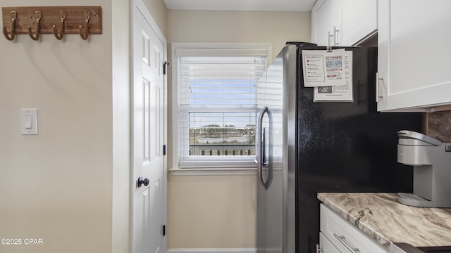 kitchen with white cabinetry, light stone counters, and stainless steel refrigerator