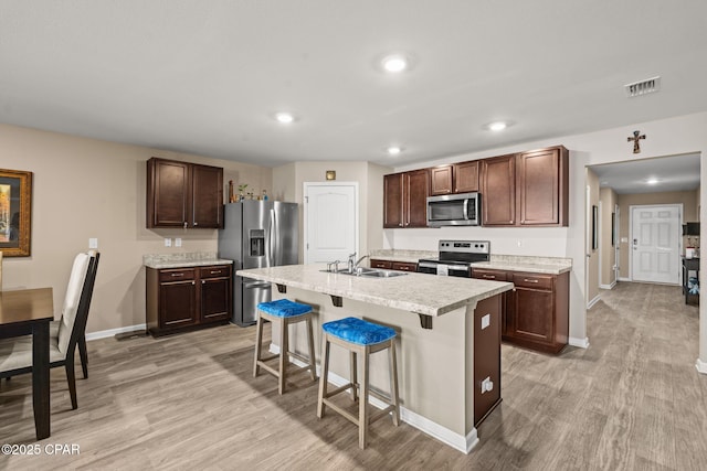 kitchen featuring appliances with stainless steel finishes, sink, a kitchen island with sink, light hardwood / wood-style flooring, and a breakfast bar area