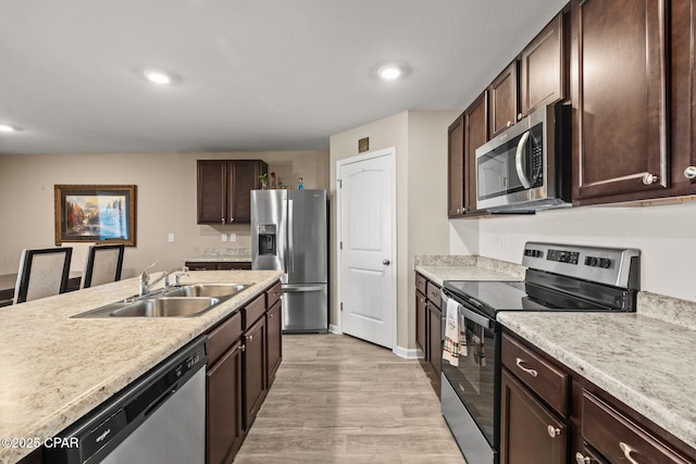 kitchen with appliances with stainless steel finishes, light hardwood / wood-style floors, sink, a kitchen breakfast bar, and dark brown cabinets