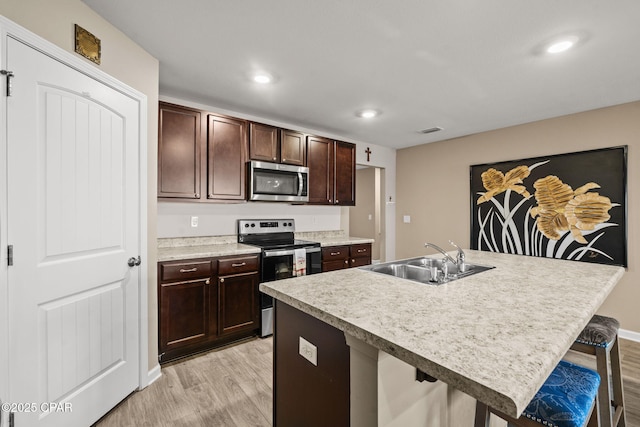 kitchen featuring appliances with stainless steel finishes, a kitchen island with sink, light wood-type flooring, a breakfast bar, and sink