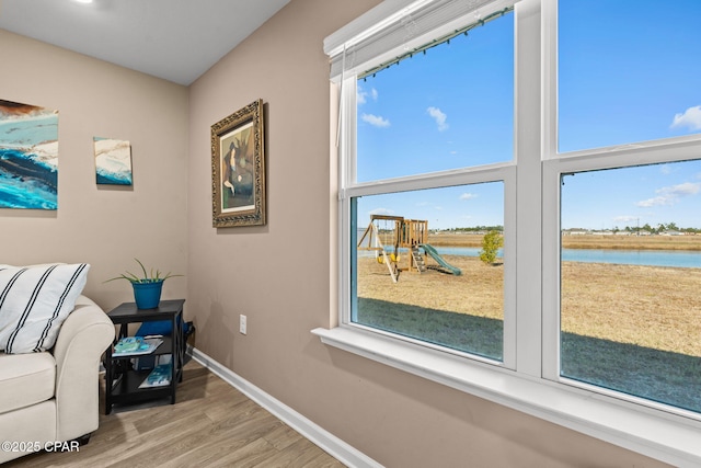 sitting room with wood-type flooring, a water view, and a healthy amount of sunlight