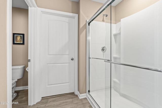 bathroom with toilet, a shower with shower door, and wood-type flooring