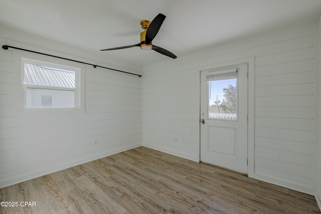 interior space with ceiling fan, wood walls, and light hardwood / wood-style floors