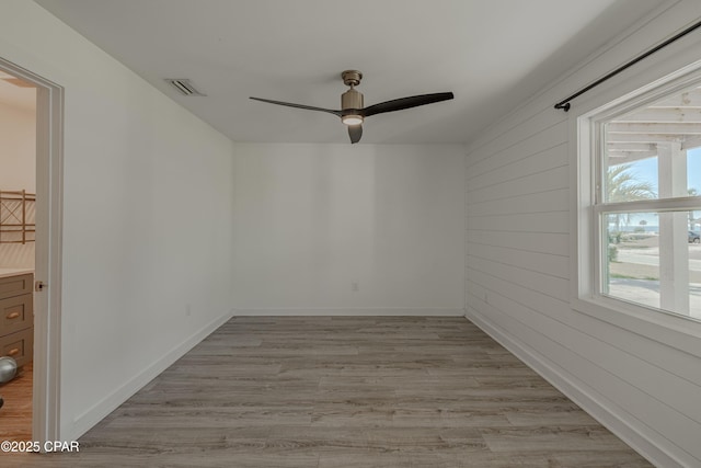 empty room with ceiling fan, wooden walls, and light wood-type flooring