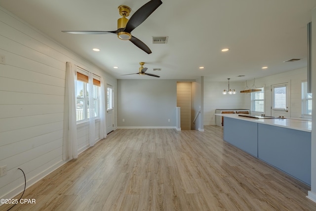 unfurnished living room featuring ceiling fan with notable chandelier, wooden walls, and light wood-type flooring