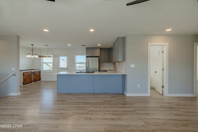 kitchen featuring decorative light fixtures, sink, gray cabinets, kitchen peninsula, and stainless steel refrigerator