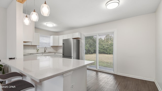 kitchen with stainless steel fridge, a breakfast bar area, white cabinetry, tasteful backsplash, and decorative light fixtures