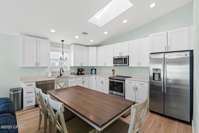 kitchen featuring vaulted ceiling with skylight, pendant lighting, appliances with stainless steel finishes, white cabinetry, and sink