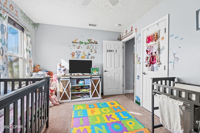 carpeted bedroom featuring a nursery area, ceiling fan, and a textured ceiling