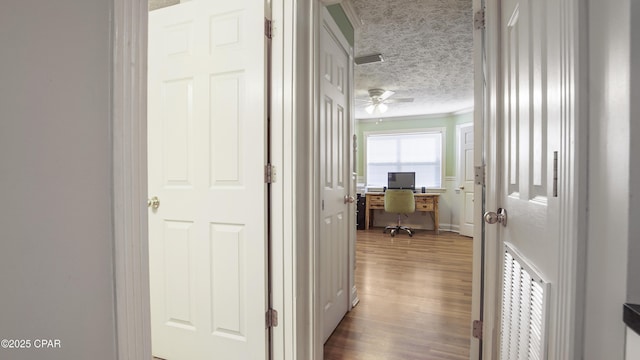 hallway with light wood-type flooring, ornamental molding, and a textured ceiling