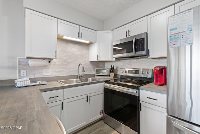 kitchen with appliances with stainless steel finishes, sink, white cabinets, and a textured ceiling