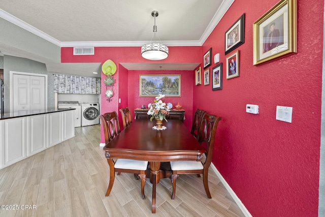 dining area featuring visible vents, ornamental molding, washing machine and dryer, light wood finished floors, and a textured wall