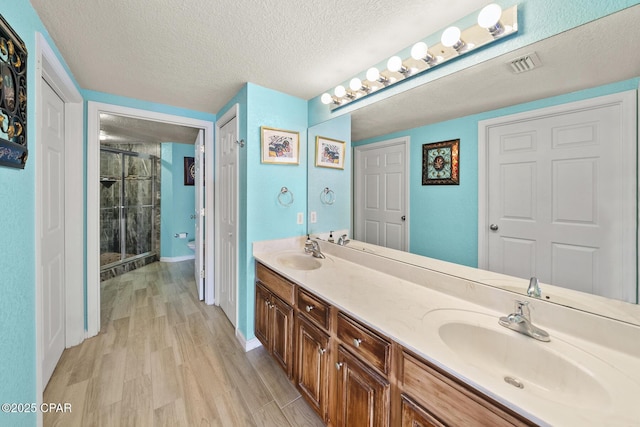 full bath featuring wood finished floors, double vanity, a stall shower, a sink, and a textured ceiling