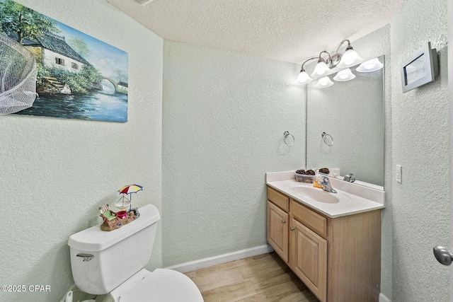 bathroom featuring a textured ceiling, toilet, vanity, and a textured wall