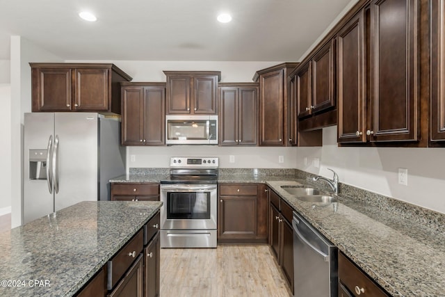 kitchen with sink, dark brown cabinets, light wood-type flooring, appliances with stainless steel finishes, and stone counters