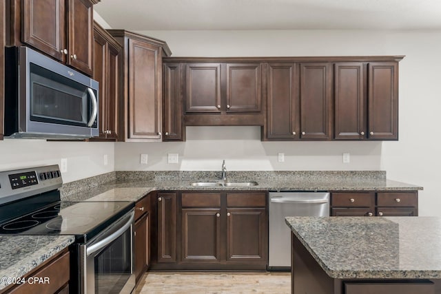 kitchen with sink, appliances with stainless steel finishes, dark stone countertops, dark brown cabinetry, and light hardwood / wood-style floors