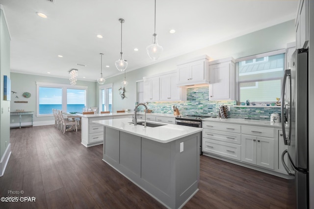 kitchen featuring a center island with sink, sink, hanging light fixtures, stainless steel appliances, and white cabinets