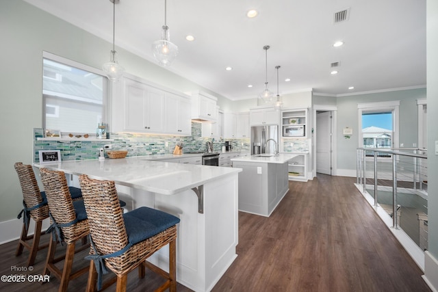 kitchen with white cabinetry, a center island with sink, a kitchen breakfast bar, dark wood-type flooring, and pendant lighting