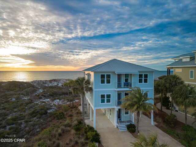 raised beach house featuring concrete driveway, a water view, metal roof, a balcony, and a carport