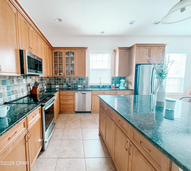 kitchen featuring sink, tasteful backsplash, dark stone counters, light tile patterned floors, and stainless steel appliances