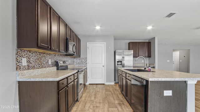 kitchen with light hardwood / wood-style flooring, an island with sink, black appliances, decorative backsplash, and sink