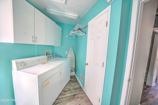 laundry room featuring a textured ceiling, cabinets, washing machine and dryer, and light hardwood / wood-style flooring