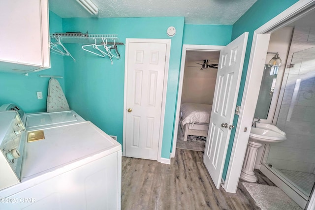 clothes washing area featuring separate washer and dryer, a textured ceiling, cabinets, sink, and light wood-type flooring