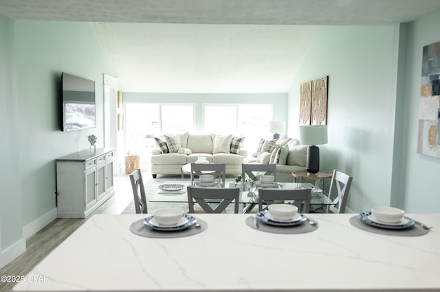 dining area with light wood finished floors, baseboards, and lofted ceiling