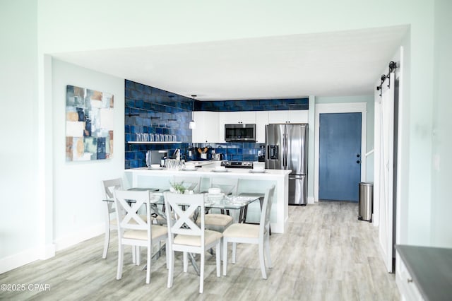 dining space featuring light wood-style flooring, baseboards, and a barn door