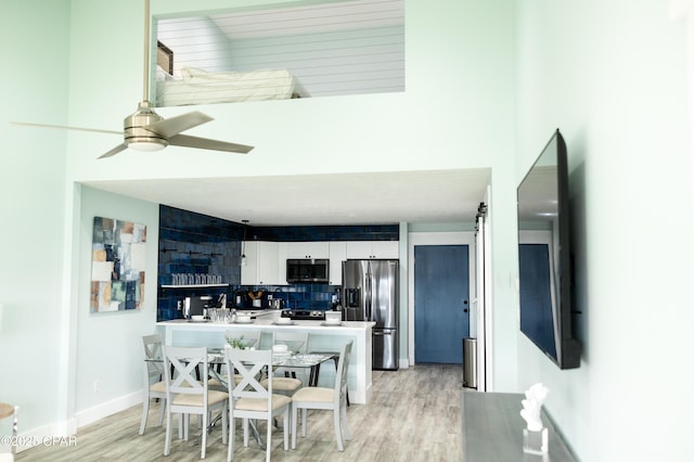 dining space with baseboards, a high ceiling, light wood-style flooring, and a ceiling fan