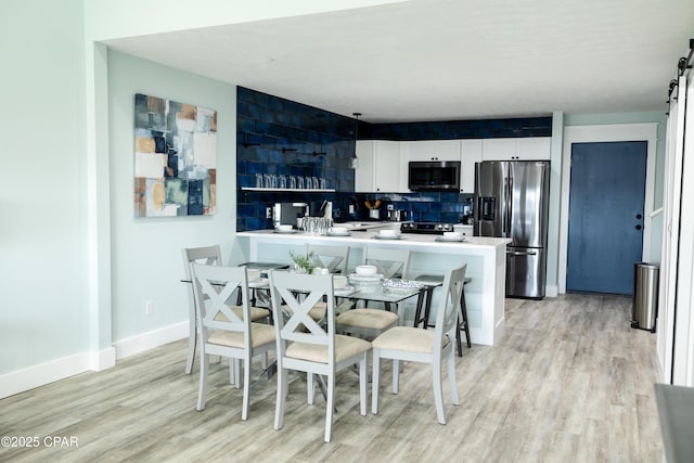 dining space with baseboards, light wood-type flooring, and a barn door