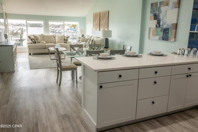 kitchen featuring light countertops, open floor plan, lofted ceiling, light wood-style flooring, and white cabinets