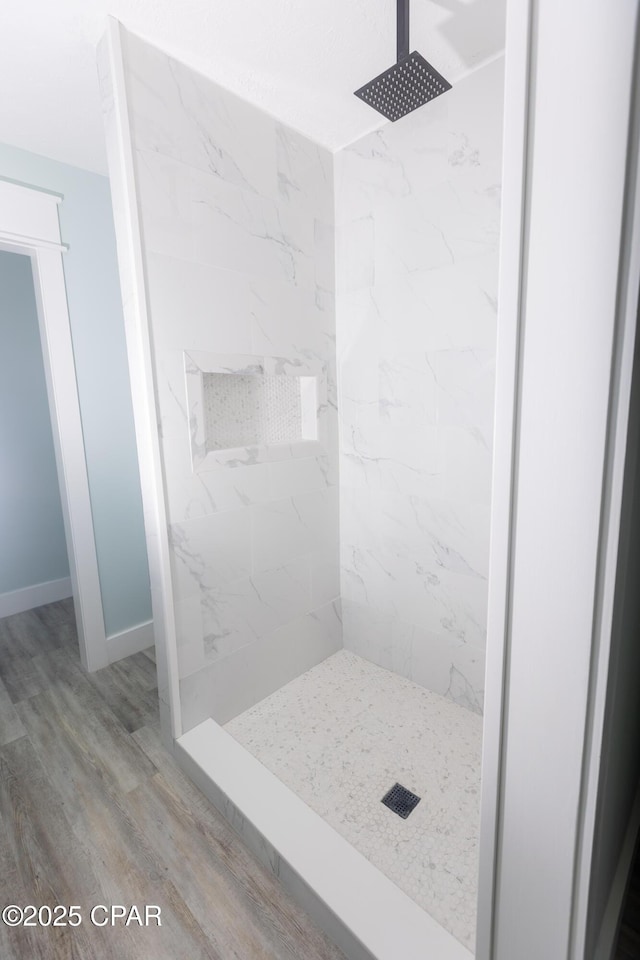 bathroom featuring baseboards, a tile shower, and wood finished floors